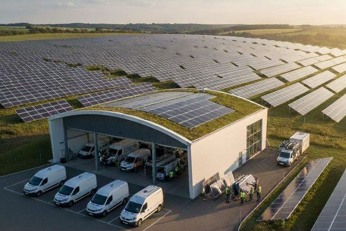 Aerial view of a large-scale solar power plant with rows of ground-mounted panels beside a service depot