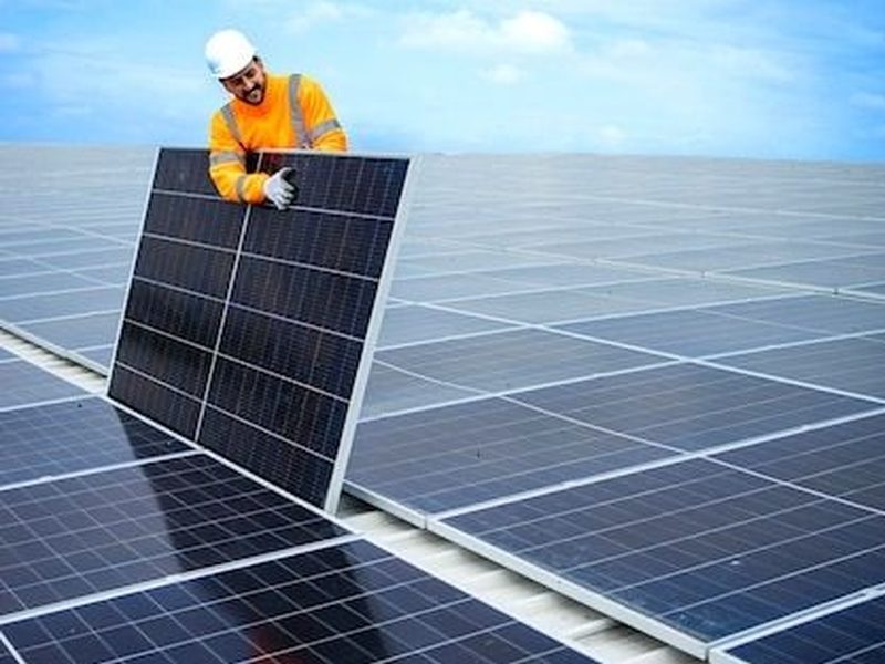 Technician positioning a solar panel on a large commercial rooftop array